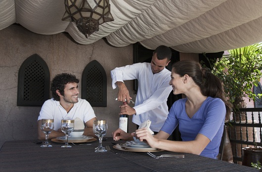 Waiter serving tourist couple red wine