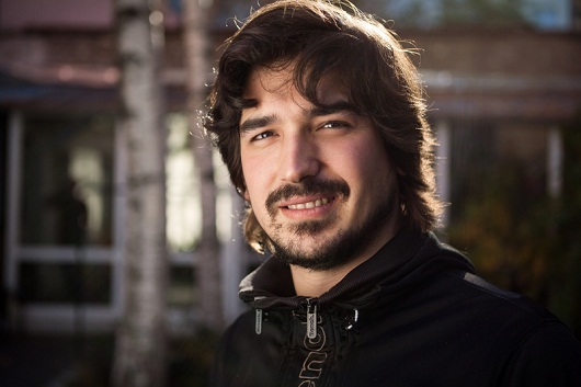 Portrait of smiling men with longer hair and beard, backlit with sun, showing teeth