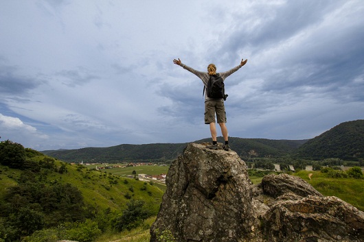 Woman standing alone on rock and raising arms.